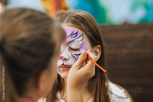 Professional make-up artist, female artist draws with pencil, brush, watercolors, makes face painting for a beautiful girl, child for Halloween. Photography, portrait.