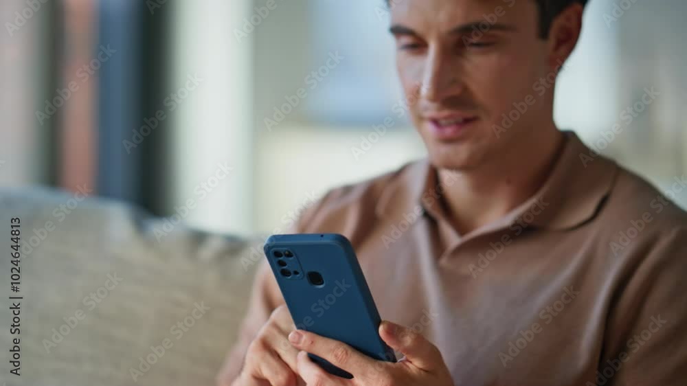 Cheerful guy looking smartphone on sofa modern apartment closeup. Smiling man