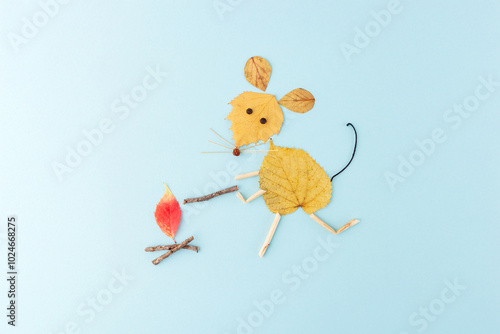 a creative and artistic composition of a mouse made from autumn leaves and twigs on a light blue background. red leaf that looks like a flame, use of natural elements , photo