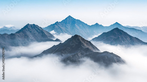 Sharp mountain peaks rising above a sea of clouds, creating a dramatic and majestic landscape under a pale blue sky.