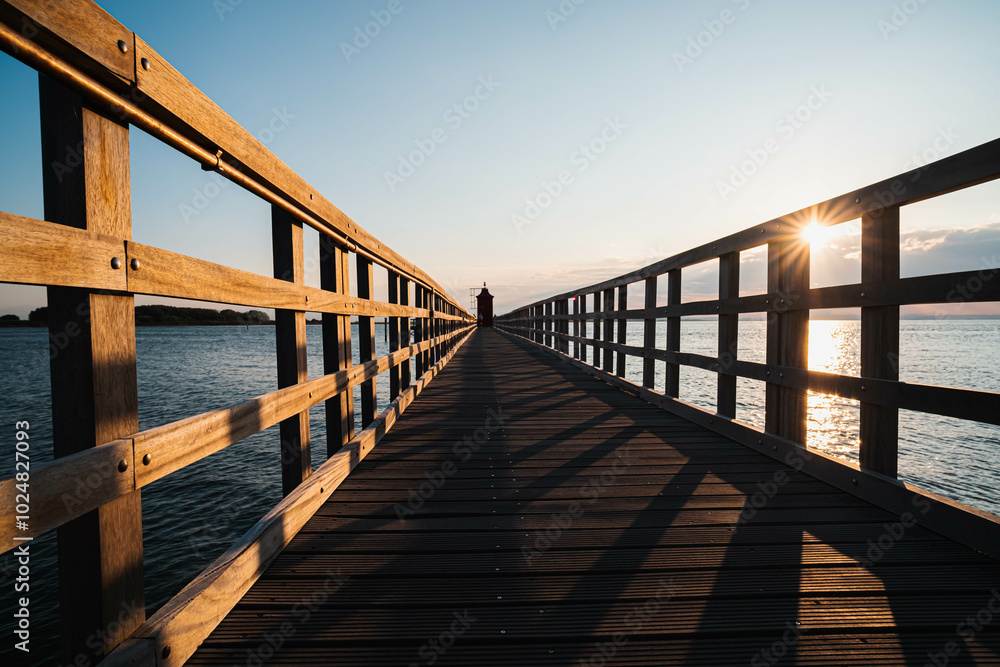 Naklejka premium The planked passage to the lighthouse on the seashore during the golden hour at dawn
