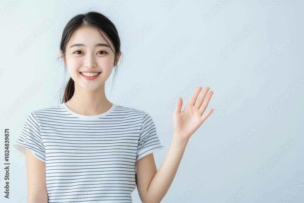 Asian teen girl waving her hand and smiling at the camera, greeting you, standing in front of a white background saying hello Asian teen girl waving her hand and smiling at the camera, greeting you, standing in front of a white background saying hello