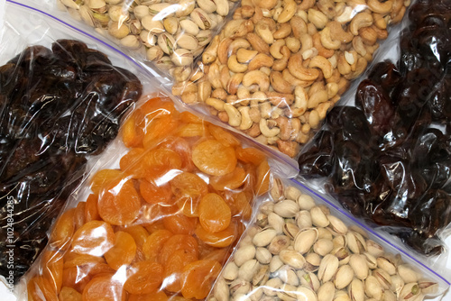 Assorted nuts and dried fruits displayed in clear bags on a white background, showcasing a variety of textures and colors for snacking or cooking
