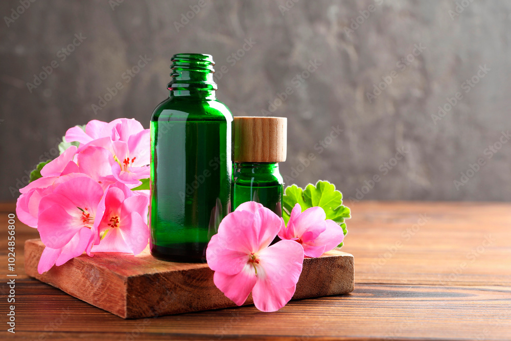 Geranium essential oil in bottles and beautiful flowers on wooden table, space for text Geranium essential oil in bottles and beautiful flowers on wooden table, space for text