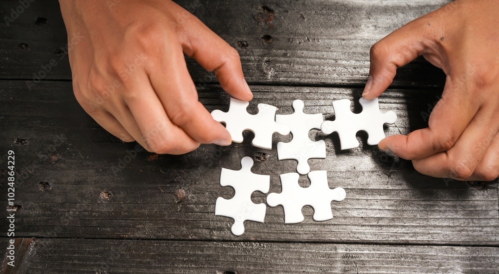 Obraz premium A group of people are putting together a jigsaw puzzle and trying to put the pieces together. This is a scene where everyone is working together on a wooden table, holding a jigsaw puzzle.