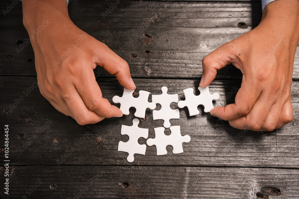 Obraz premium A group of people are putting together a jigsaw puzzle and trying to put the pieces together. This is a scene where everyone is working together on a wooden table, holding a jigsaw puzzle.