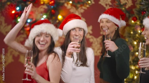 Four women dance on in front of Christmas decoations with champagne and santa harts photo