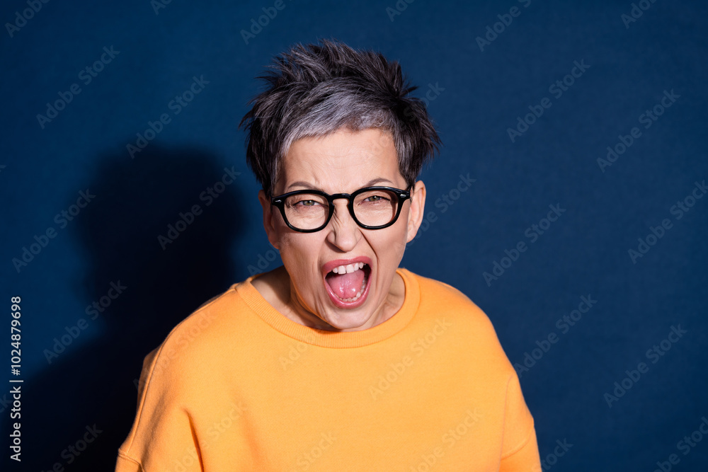 Photo portrait of pretty senior female annoyed scream angry wear trendy yellow outfit isolated on dark blue color background Photo portrait of pretty senior female annoyed scream angry wear trendy yellow outfit isolated on dark blue color background