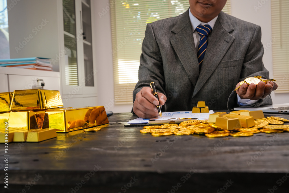 Businessman doing online gold transactions emphasizes the convenience of investing in digital gold. Businessman holds shiny gold bars in office, symbolizing wealth and investment opportunities. Businessman doing online gold transactions emphasizes the convenience of investing in digital gold. Businessman holds shiny gold bars in office, symbolizing wealth and investment opportunities.