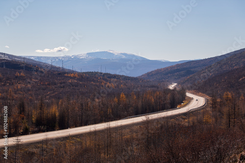 Winding road among the mountains. Autumn landscape with an asphalt road. A car is driving in the distance. Kolyma highway, Magadan region, Russia. Car trip through Siberia and the Russian Far East. photo