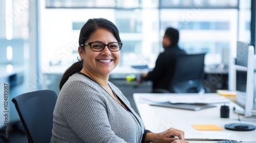 Free Download Employee seated at a desk, smiling in a modern office, with a coworker in the background. Simple scene with minimal distractions. - GFXLoad