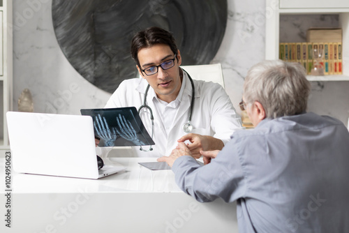 Old man visiting young male doctor rheumatologist in modern clinic	
