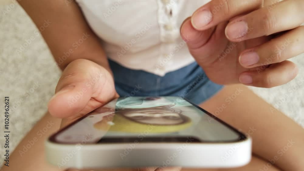Point of view, high angle shot of woman sitting cross-legged on carpet using her smartphone, scrolling photos, zooming in with two fingers Point of view, high angle shot of woman sitting cross-legged on carpet using her smartphone, scrolling photos, zooming in with two fingers