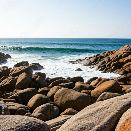 A rugged, rocky beach where large boulders line the shore, and waves crash dramatically against them. The powerful movement of the water contrasts with the clean white sky