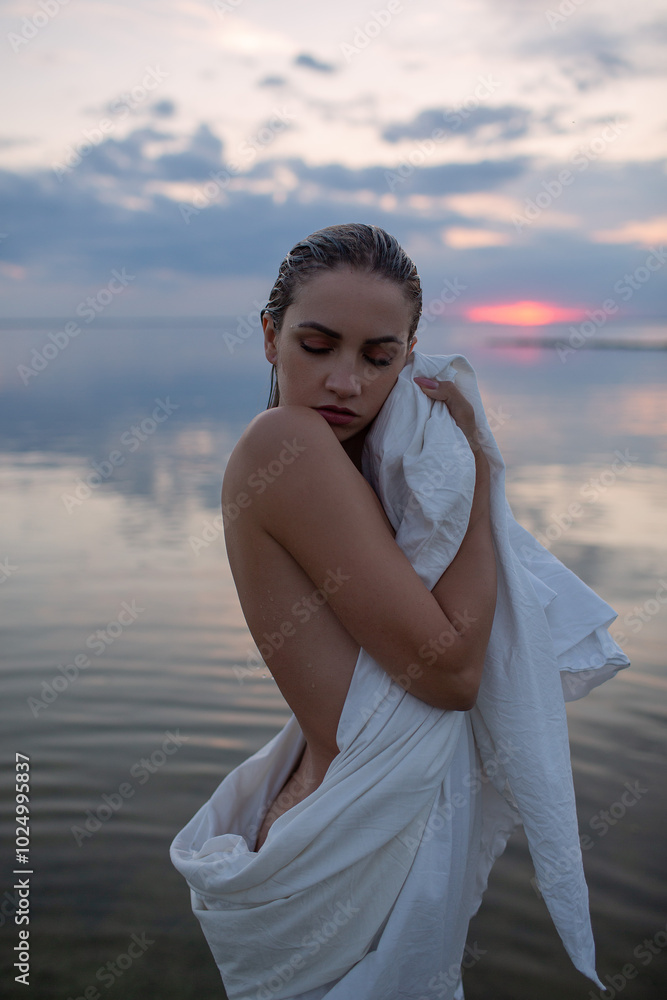 Beautiful naked woman standing in a lake at sunset, wrapped in a white sheet. Harmony with nature. Beautiful naked woman standing in a lake at sunset, wrapped in a white sheet. Harmony with nature.
