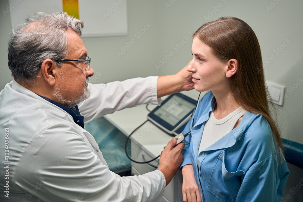 Caucasian doctor conducting ear examination on patient Caucasian doctor conducting ear examination on patient