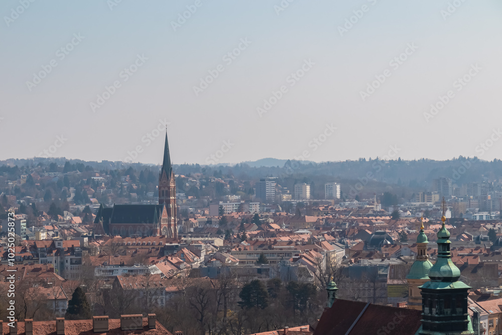 Fototapeta premium Scenic aerial view of Graz seen from Schlossberg, Styria, Austria, Europe. Unesco world heritage site with red-roofed buildings. Majestic church Herz Jesu Kirche in distance. Vibrant cityscape scene