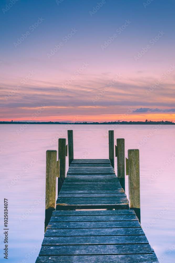 Fototapeta premium Wooden jetty and sunshine through clouds. Wooden pier at a lakeside.