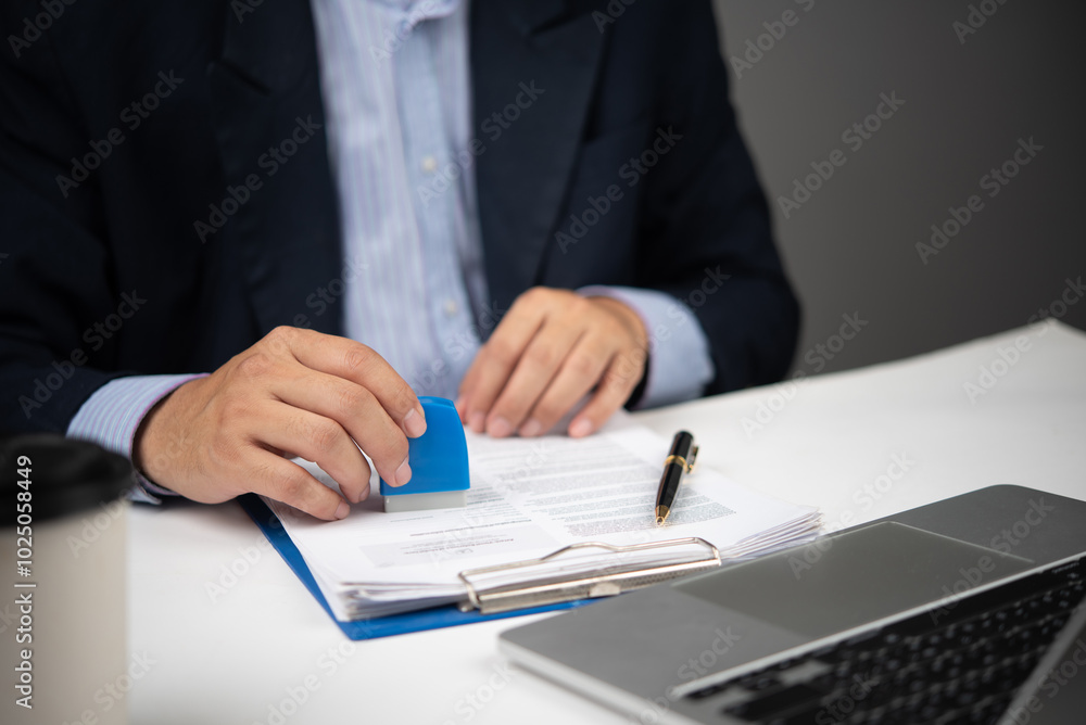 A businessman uses a stamp to approve or sign documents, representing official business or legal processes. A businessman uses a stamp to approve or sign documents, representing official business or legal processes.