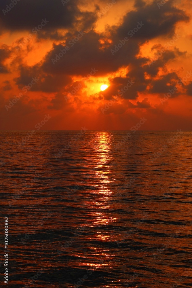 Fototapeta premium Romantic morning by the sea. Vivid rising red sun, calm morning water surface under the dark clouds. Distant dark sky, water and colorful sunrise. Morning by the ocean, travel landscape photography. 