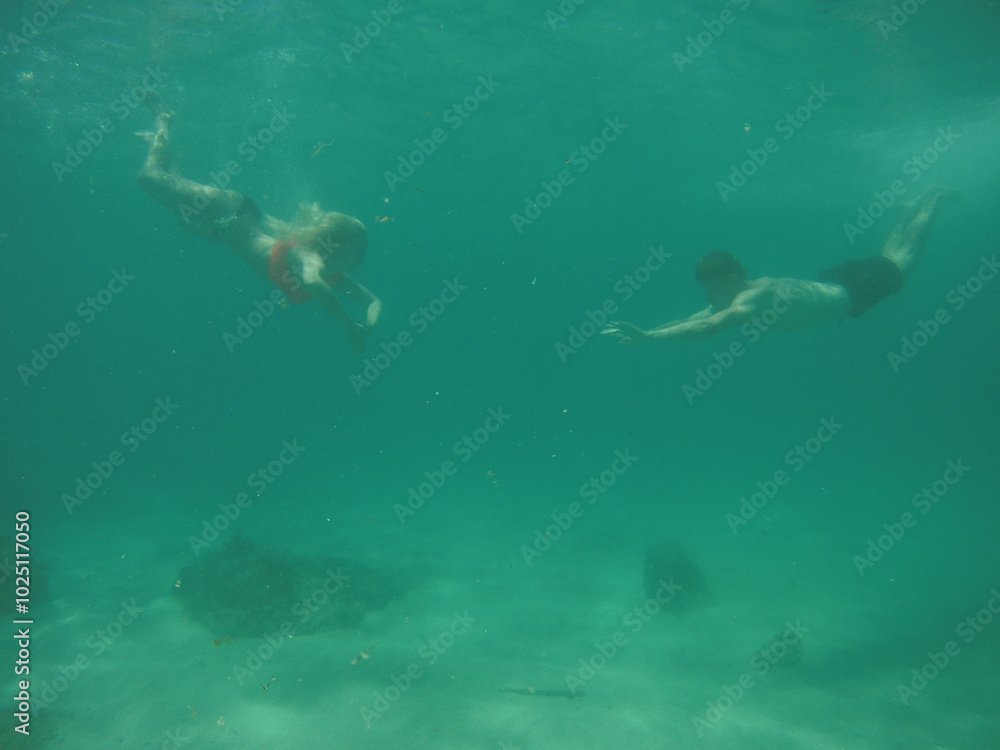 Beautiful young woman with long hair dressed in white swimsuit swims deep under the crystal azure water of caribbean sea, man diving underwater in black shorts Beautiful young woman with long hair dressed in white swimsuit swims deep under the crystal azure water of caribbean sea, man diving underwater in black shorts