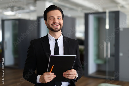 A man in a suit holding a clipboard and a pencil. He is smiling and he is happy