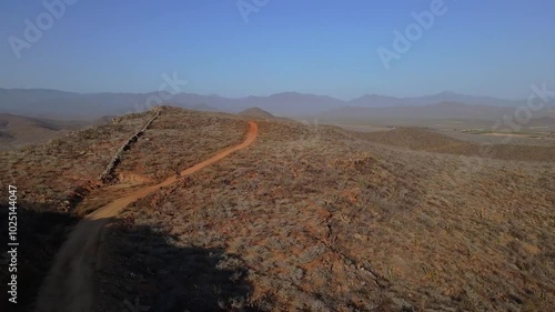 Wallpaper Mural Aerial drone footage of a mountain biker pedalling up a red dirt road in the desert surrounded by bushes on a clear day Torontodigital.ca