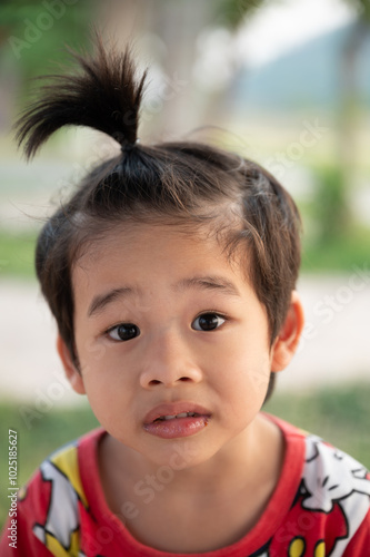 Young child with a playful hairstyle outdoors in a green natural setting on a sunny day enjoying childhood moments