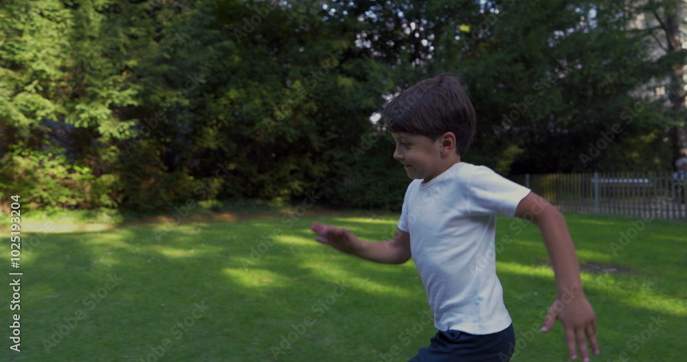 Young boy running in a park, wearing a white shirt, with a determined expression, surrounded by greenery, enjoying an energetic moment outdoors on a sunny day Young boy running in a park, wearing a white shirt, with a determined expression, surrounded by greenery, enjoying an energetic moment outdoors on a sunny day