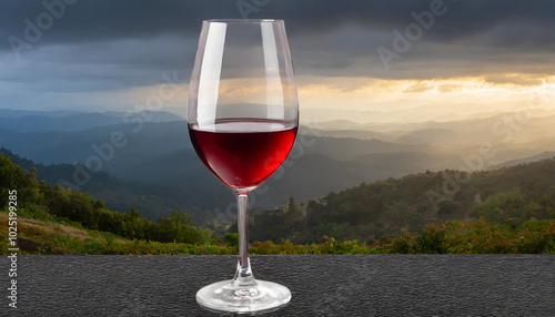 A glass of red wine rests on a table, overlooking a scenic mountain landscape at sunset with dramatic clouds