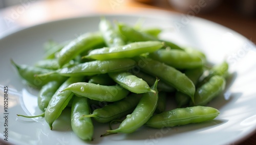 Fresh green snap peas on white plate glistening with water droplets in soft natural light