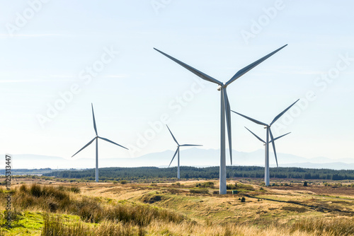 Wind farm turbines in wild Scottish moor land countryside with Isle of Arran in background on hazy day