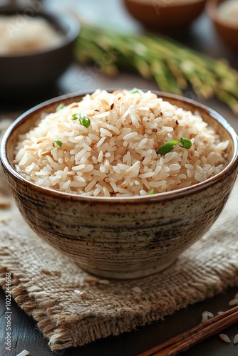 A bowl of rice on burlap cloth, with stalks of rice plants, white background