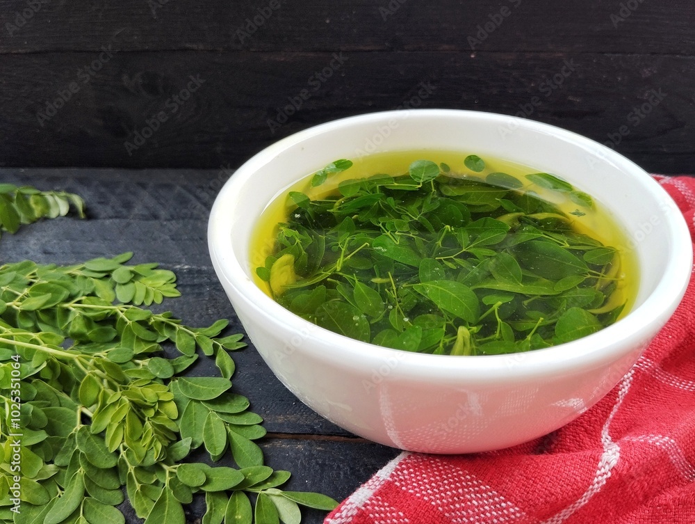 Moringa leaves soup in bowl on the black wooden table. Herb medicine plant, Organic farm plant Moringa leaves soup in bowl on the black wooden table. Herb medicine plant, Organic farm plant