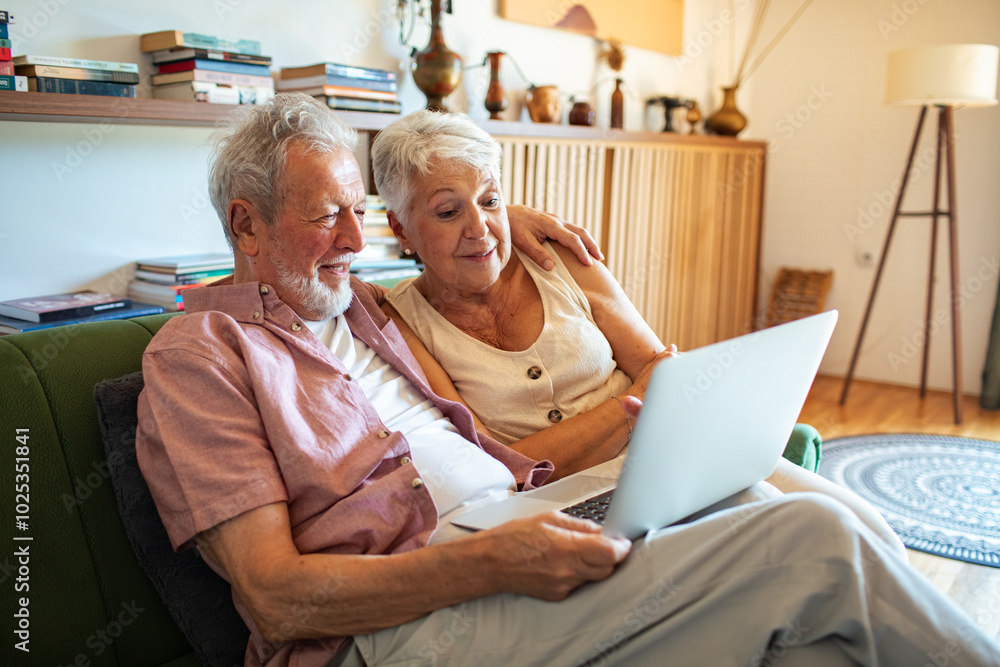 Obraz premium Happy senior couple using laptop together on a couch at home