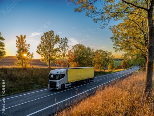 Obraz na płótnie Silver truck driving on an asphalt road between rows of leafy trees in autumn colors in a rural landscape at sunset w salonie