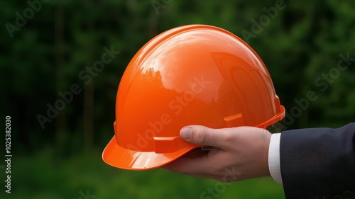 Orange safety helmet held by hand, blurred green background.