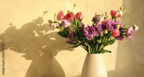 Vase with beautiful eustoma flowers near beige wall, closeup. Space for text