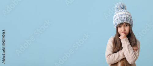Sad little girl in winter clothes on color background