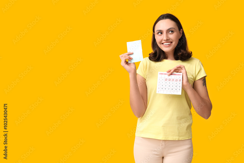 Beautiful young woman holding pad and calendar with marked days of menstruation on yellow background Beautiful young woman holding pad and calendar with marked days of menstruation on yellow background
