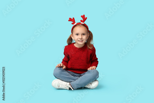 Happy little girl in reindeer horns on blue background