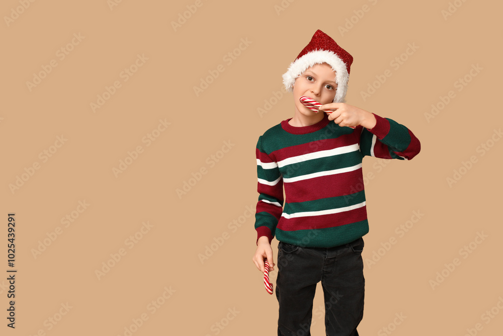 Cute little boy in Santa hat with candy canes on beige background Cute little boy in Santa hat with candy canes on beige background