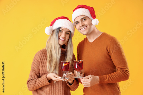 Happy young couple in Santa hats with mulled wine on yellow background