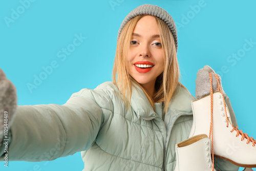 Beautiful young woman with ice skates taking selfie on blue background photo