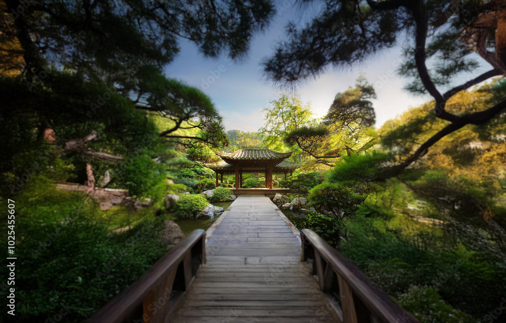 A wooden bridge leads to a gazebo in a lush green garden. A wooden bridge leads to a gazebo in a lush green garden.