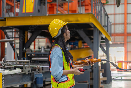 A young mechanical engineer is using a remote control to operate a crane or robot in a metal factory. Female technical worker is operating a metal production machine through a remote control