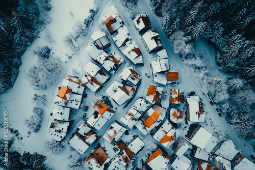 snowy winter village aerial view with orange roofs and forest trees