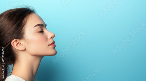 A young woman engages in a moment of mindfulness, eyes closed and face calm, promoting tranquility and mental health awareness against a soft blue backdrop, copy space