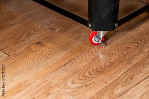 Close-Up of Table Leg with Red Wheel on Wooden Floor