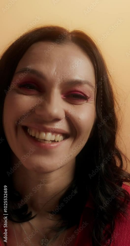 A woman with pink arrows on her eyes, dressed in casual clothes, smiles looking at the camera standing on an orange background in the studio A woman with pink arrows on her eyes, dressed in casual clothes, smiles looking at the camera standing on an orange background in the studio